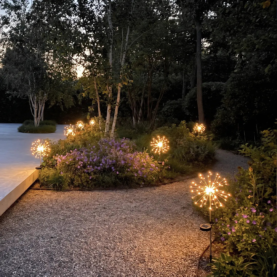 Starburst garden lights illuminating a gravel path and flowering garden beside a modern patio.