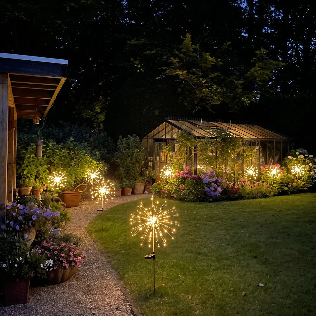 Starburst garden lights glowing along a curved lawn path beside colorful flower beds at night.