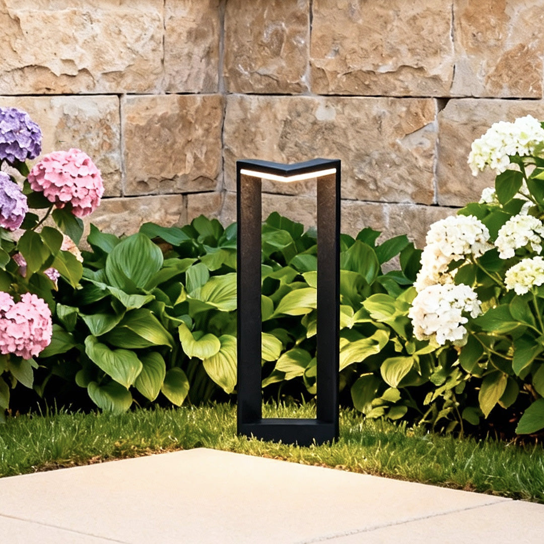 Black square bollard light positioned near stone landscaping for modern outdoor accent lighting.