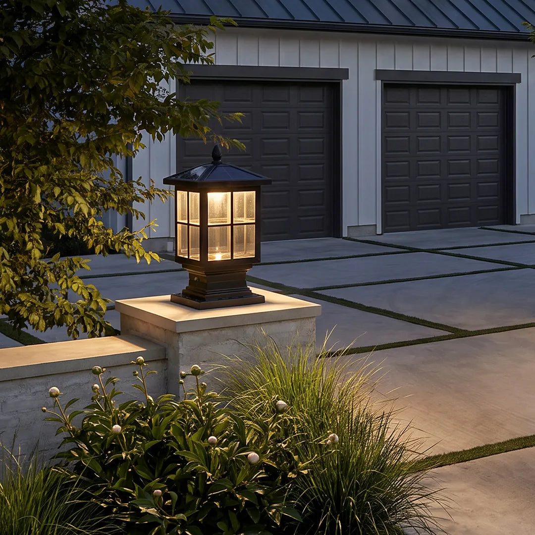 Stone light pillar installed on a square stone post near a driveway with warm lantern illumination.