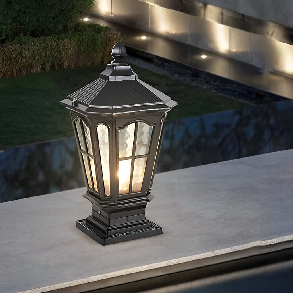 Black stone pillar light fixture mounted on low wall beside walkway providing warm and even illumination.