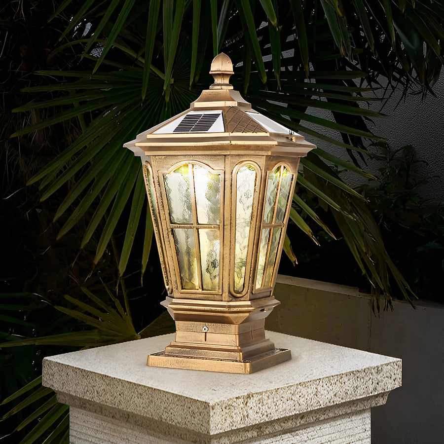 Antique bronze stone pillar light fixture with decorative frame installed on stone column surrounded by plants.