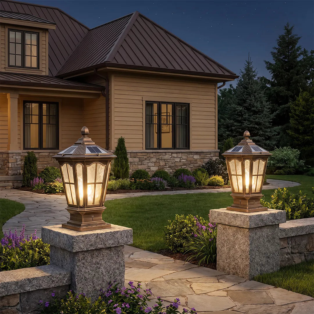 Stone pillar light fixture mounted on granite columns, illuminating a landscaped entry path in front of a traditional home at night.