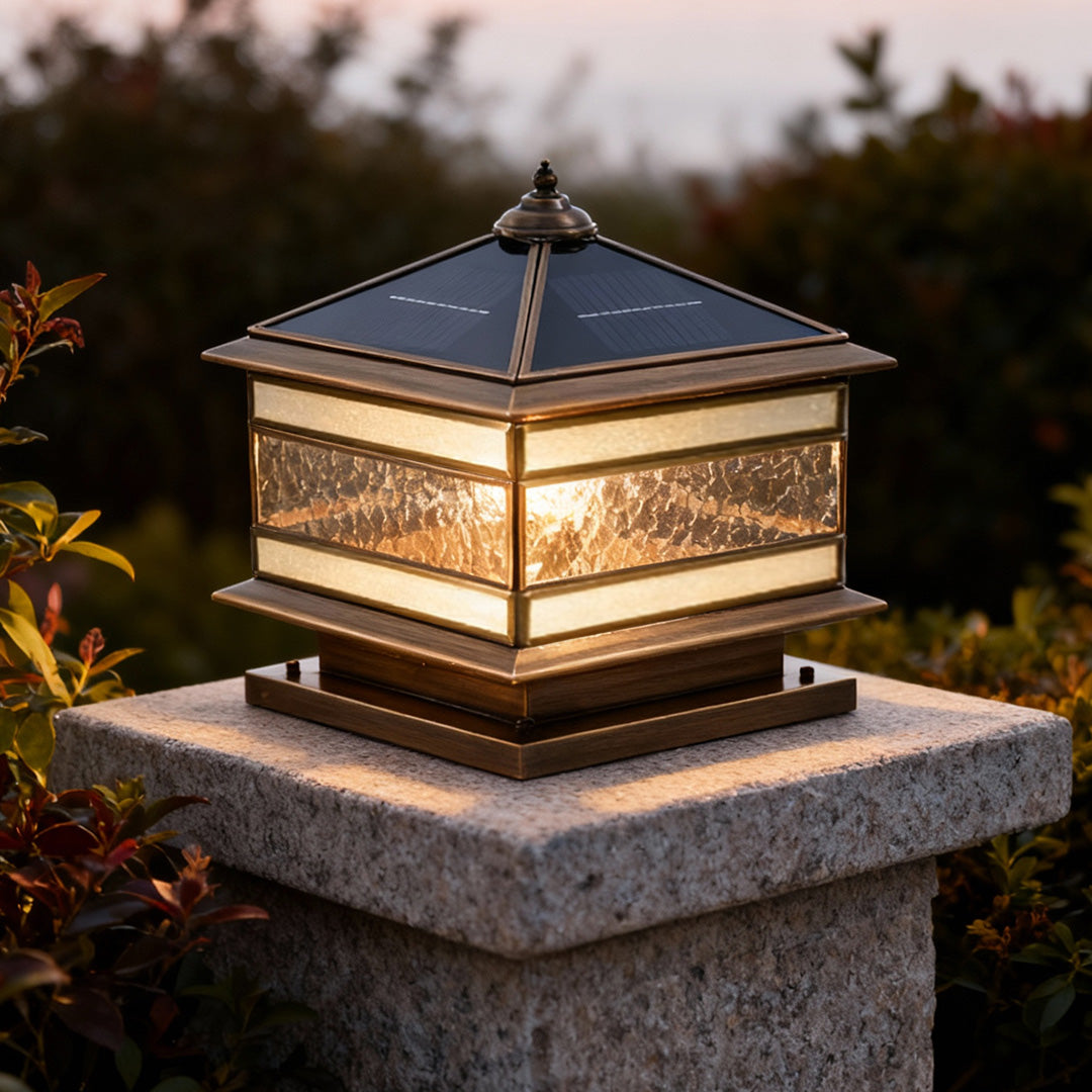 Illuminated stone pillar solar light on a square column in a landscaped yard.