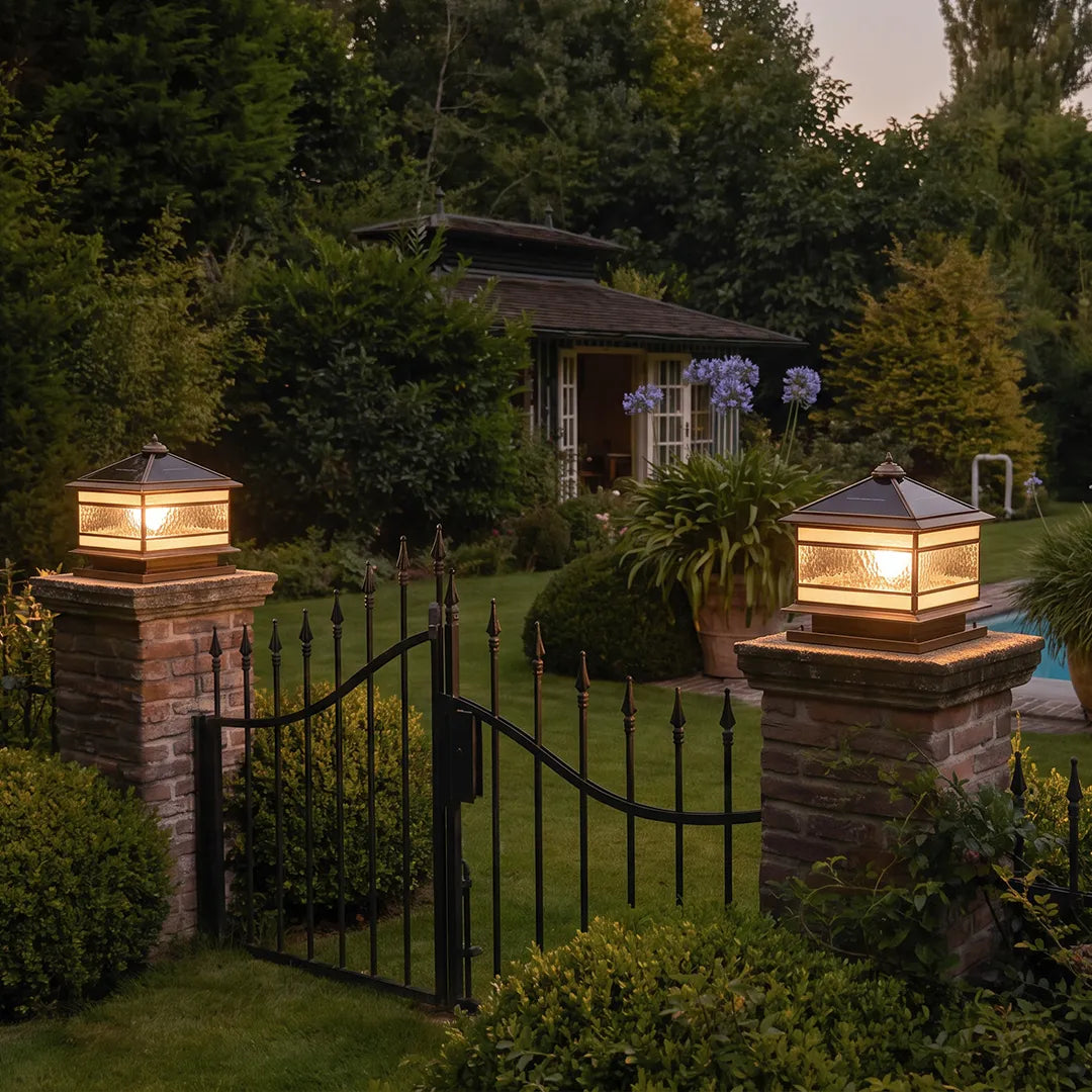 Stone pillar solar lights glowing on brick gate posts beside a garden entrance at dusk.