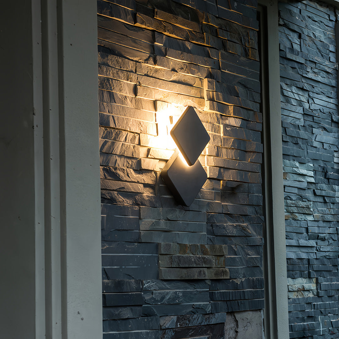 Decorative outdoor lighting sconce installed on a stone wall, creating a warm halo effect and enhancing the textured surface.