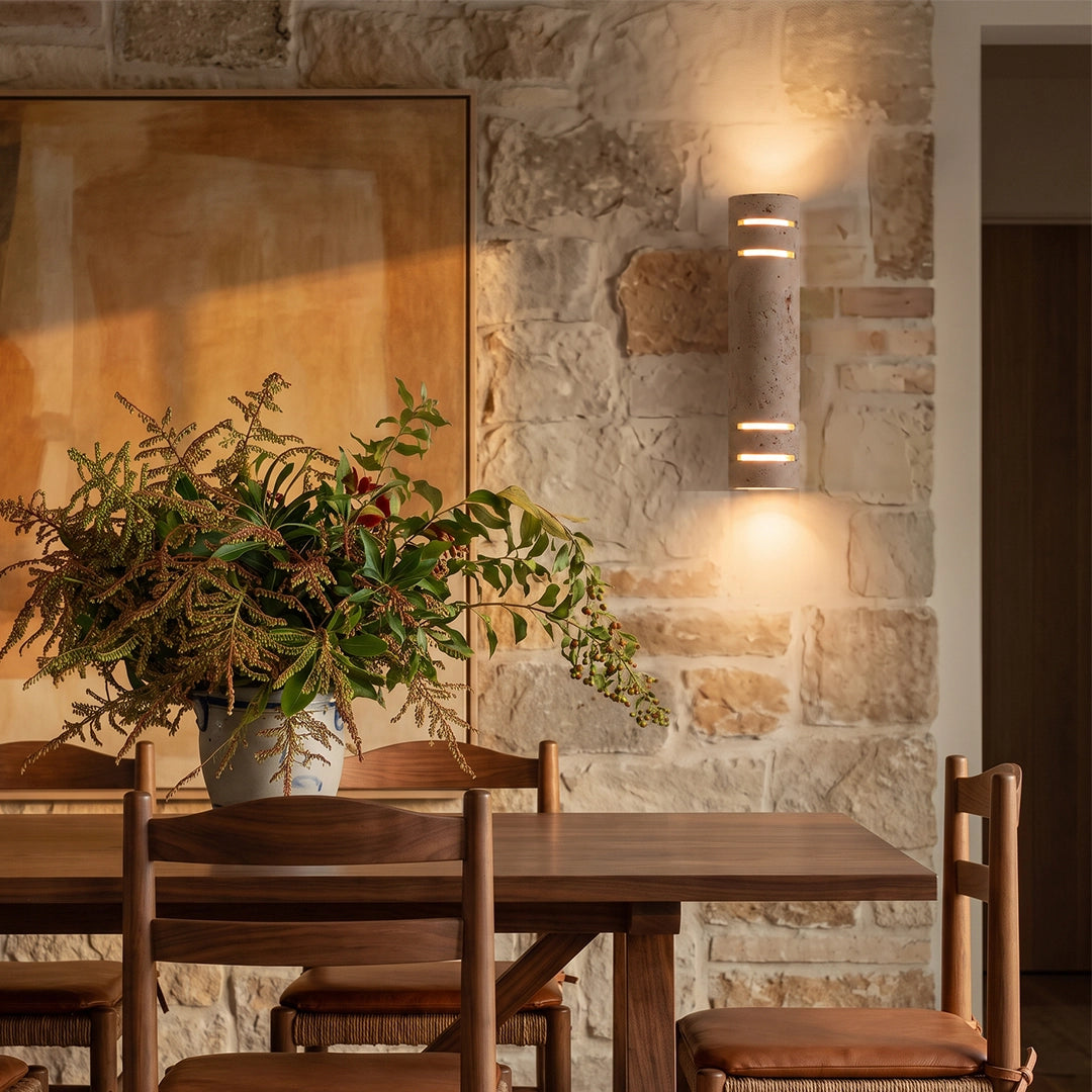 Stone wall light installed on a textured wall beside a dining table, providing warm accent lighting in a rustic room.