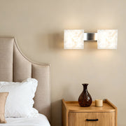 Pair of stone wall sconce lighting fixtures beside bed with neutral linens and wooden nightstand