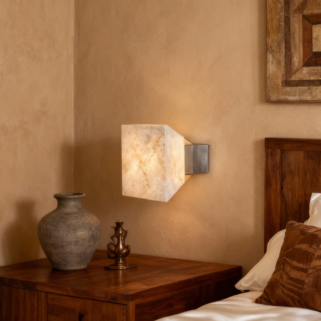 Stone wall sconce lighting creating warm glow on textured wall beside rustic wooden furniture and pottery
