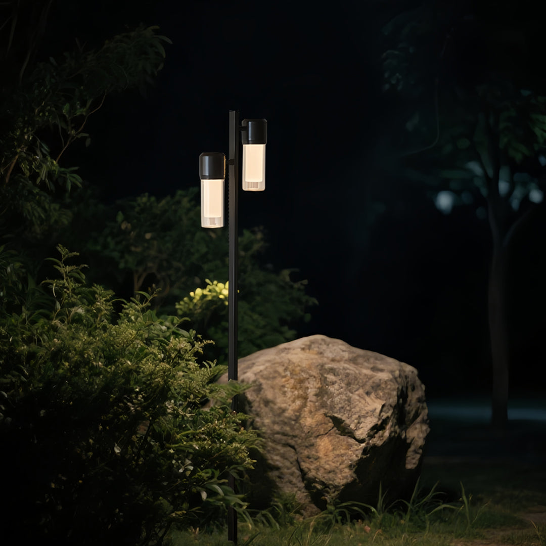 Single contemporary path light standing beside a stone path surrounded by greenery during evening.