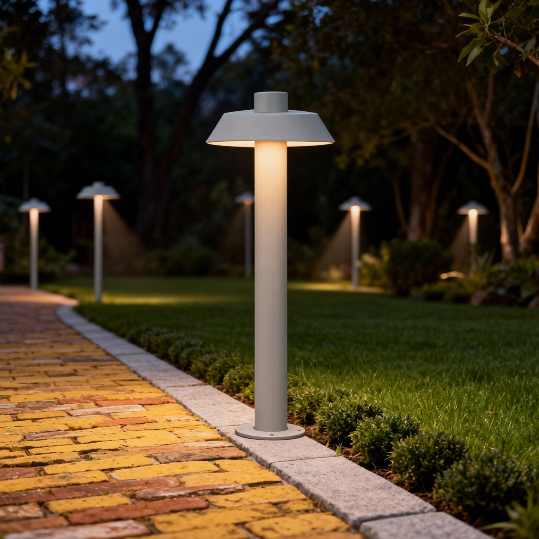 Bright silver aluminum path lights illuminating a stone walkway edged with lush green shrubs.