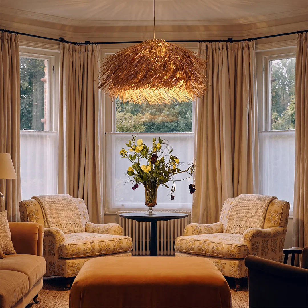 Straw pendant light suspended above a cozy sitting area with upholstered chairs and warm neutral tones.