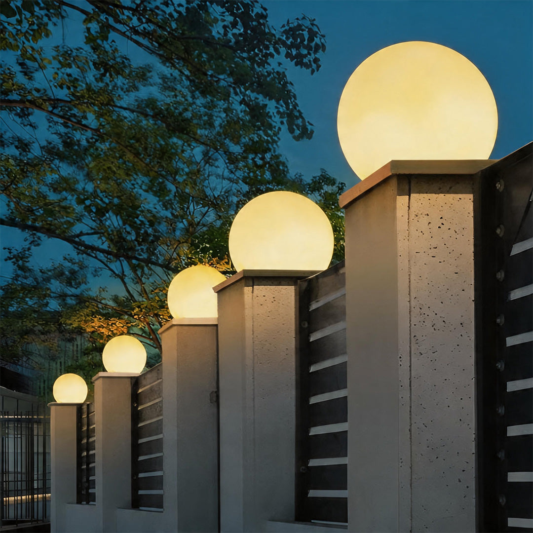 Stunning moon pillar lights of various sizes mounted on concrete posts along a garden fence.