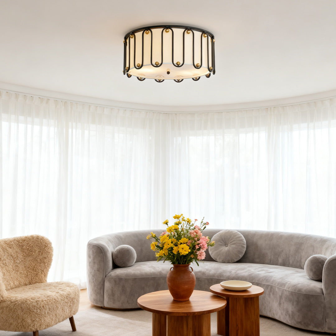 Stylish drum ceiling light flush mount with a black and gold metal cage, illuminating a cozy living room with a curved gray sofa.