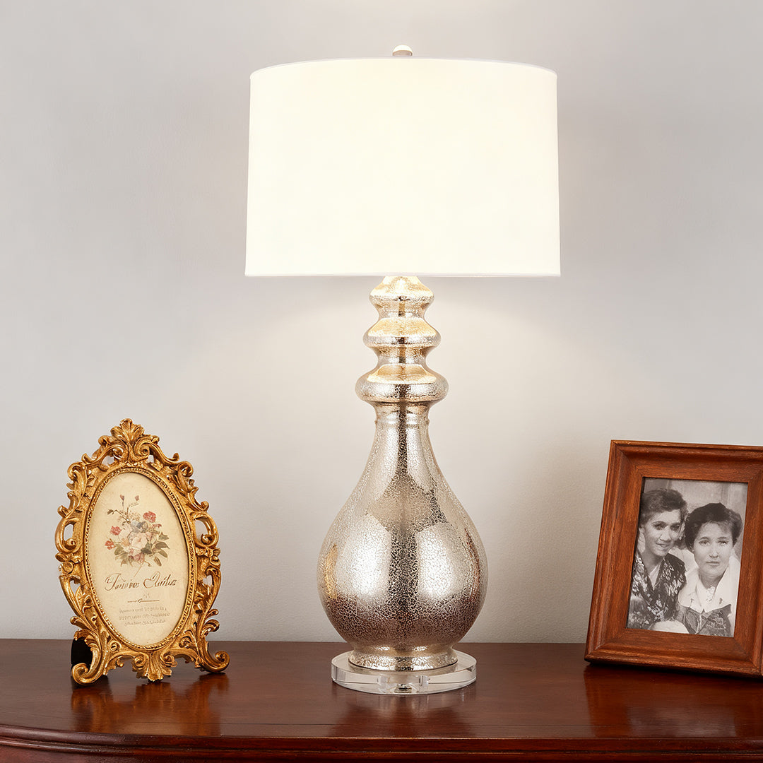 Close-up of a stylish modern silver table lamp placed on a dresser, framed by two decorative picture frames.