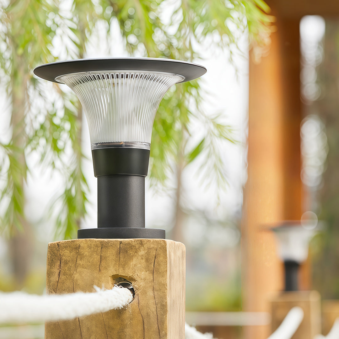 Stylish fence post cap lights fixture with a clear diffuser, mounted on a rustic wooden post with a rope railing.