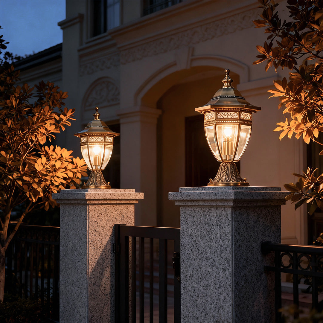 Stylish glass pillar light with intricate gold design, illuminating a stone fence for a refined outdoor atmosphere.