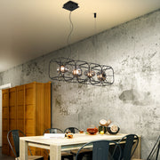 Stylish square cage chandelier hanging in industrial-modern dining room with concrete wall features