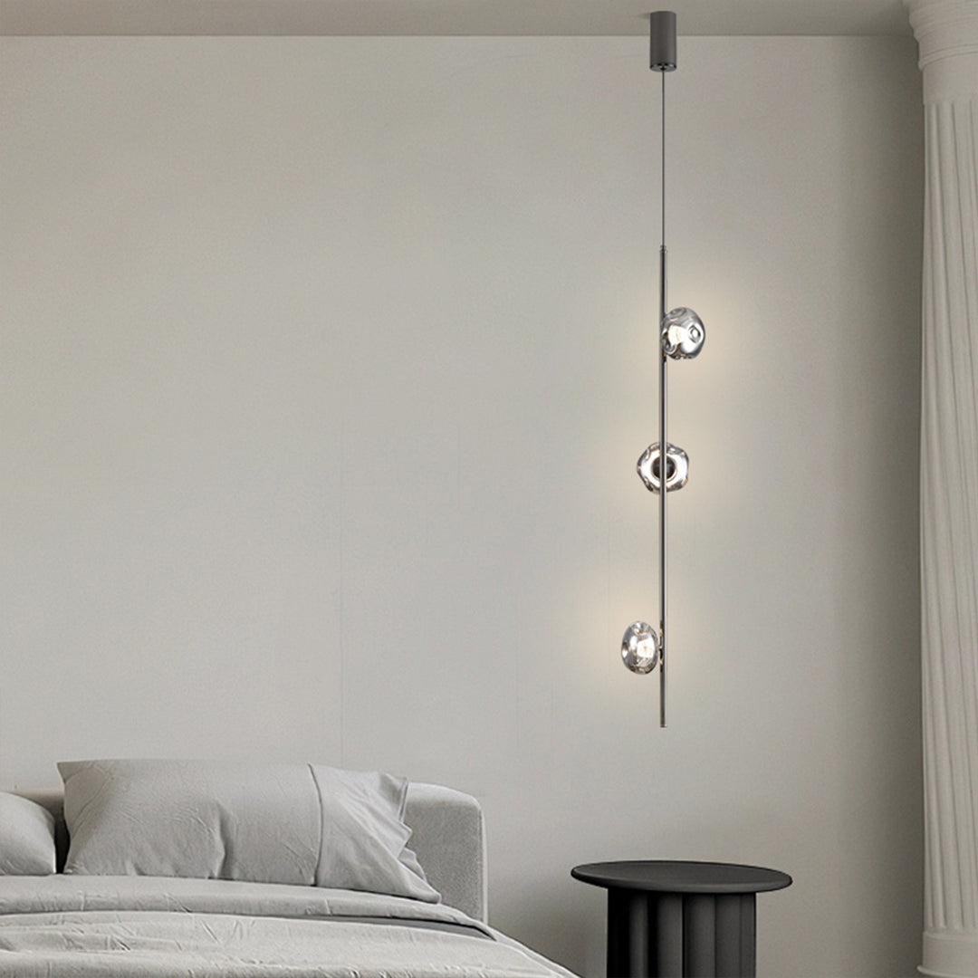 Stylish modern vertical pendant light positioned in minimalist bedroom with cascading glass elements
