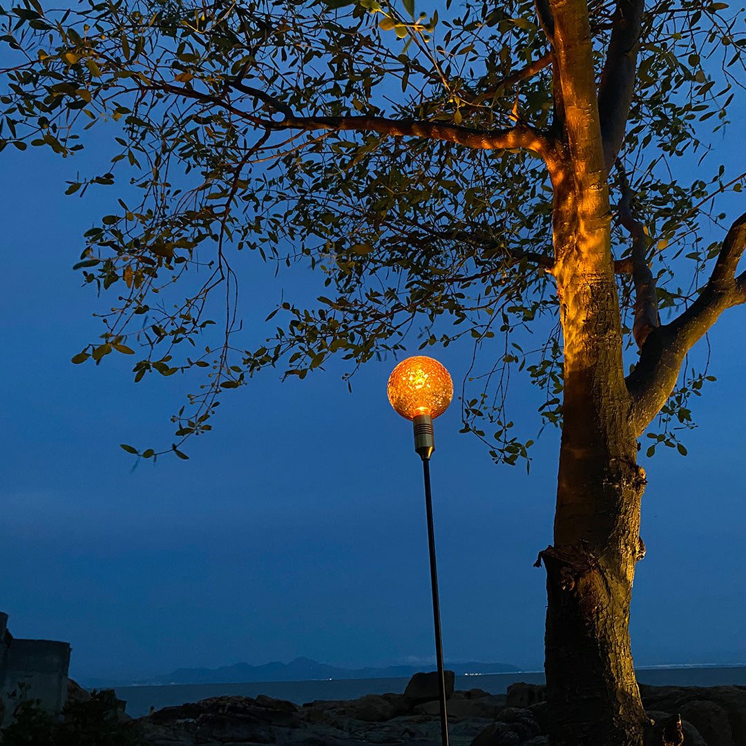 Amber globe garden stake light shining brightly at sunset for path landscape lighting.