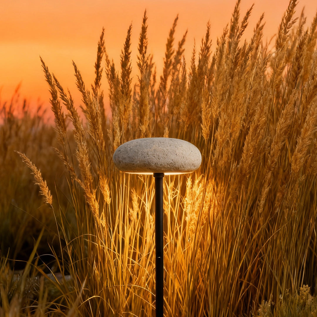 Tall white mushroom pathway light installed among tall orange grass, glowing warmly at sunset.