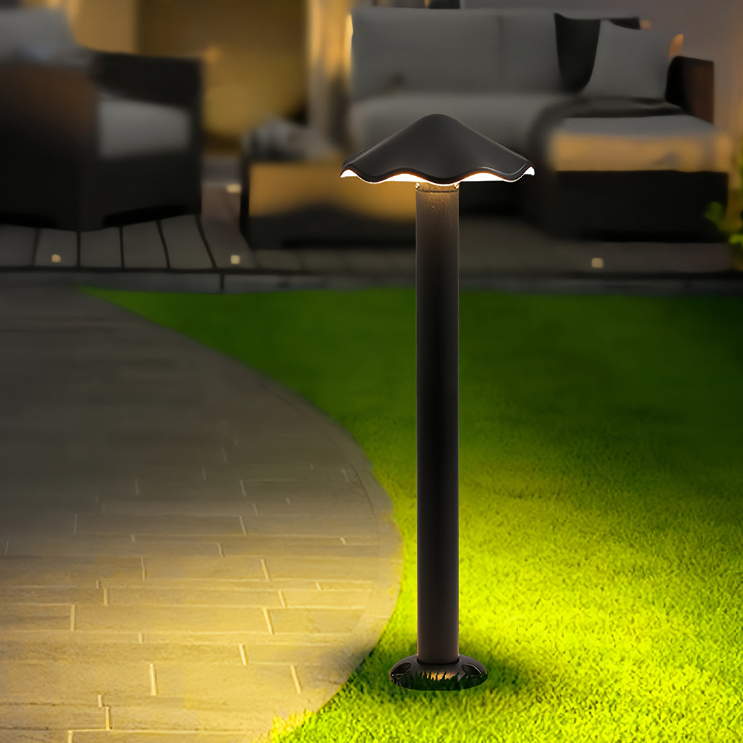 Single tall black metal pathway lights fixture illuminating a curved stone patio and seating area in an evening garden.