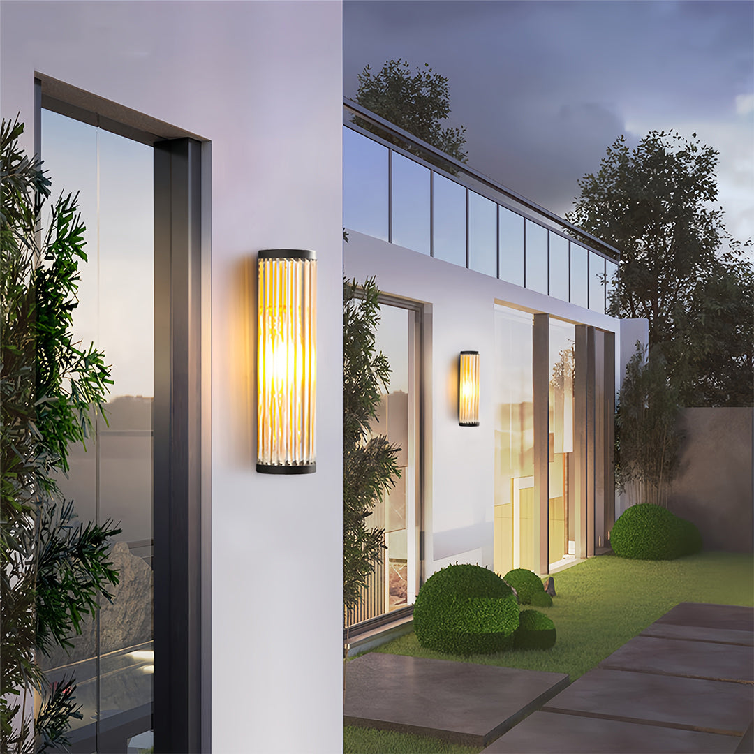 Tall cylindrical outdoor wall LED light with ribbed or fluted glass, mounted on a white exterior wall of a modern villa.