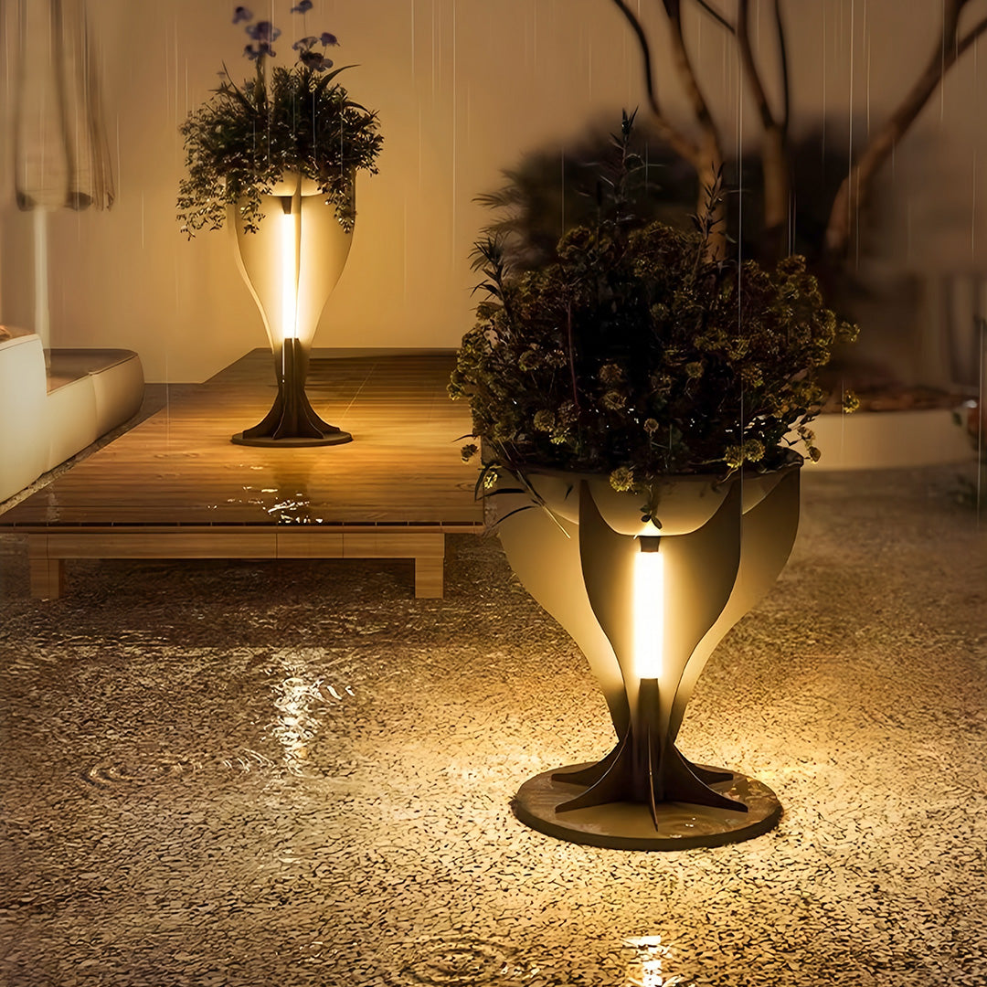 Tall, elegant lighted planter casting a warm ambient glow on a gravel patio area at night.