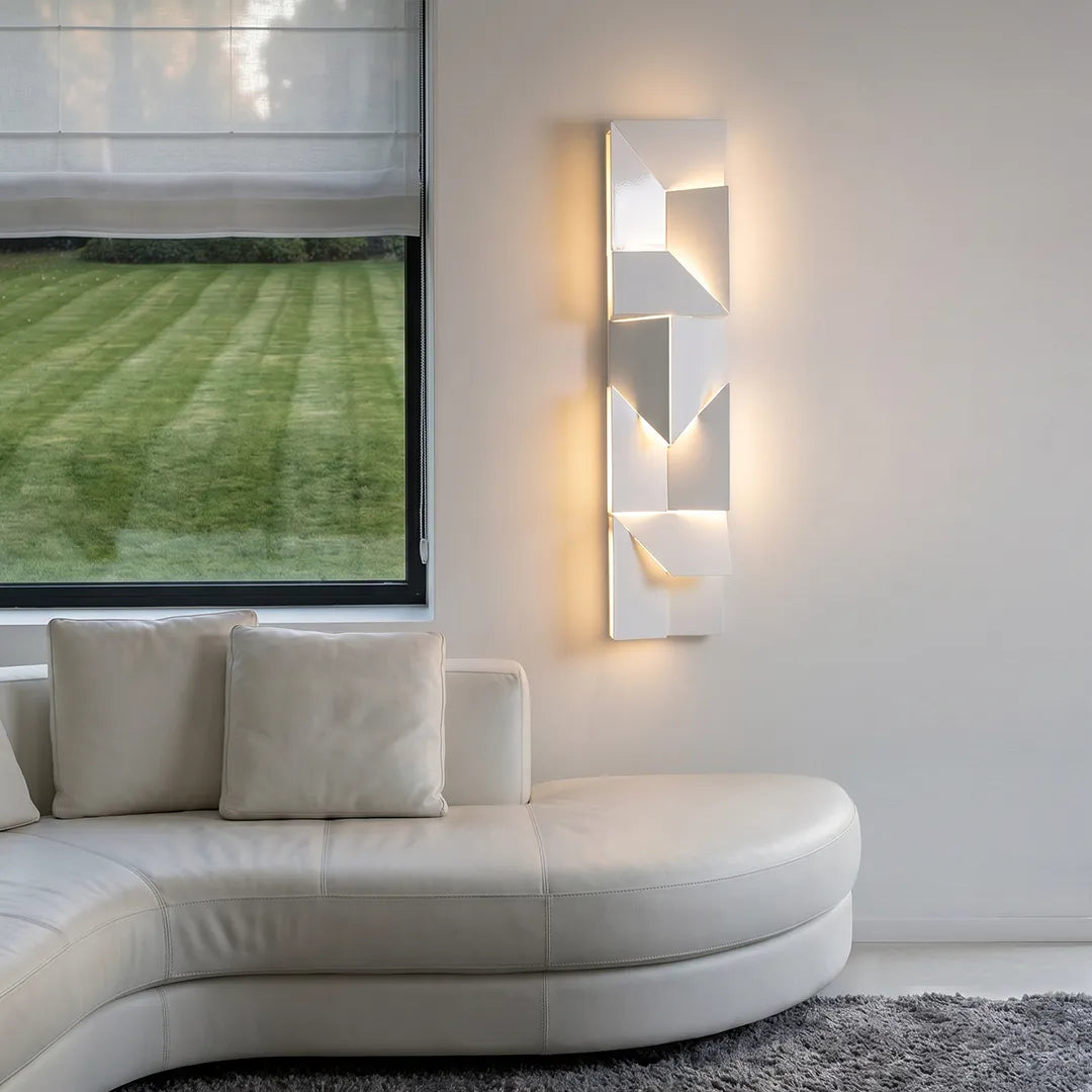 Tall geometric wall sconce light with layered illuminated panels creating a decorative statement in a contemporary sitting area.