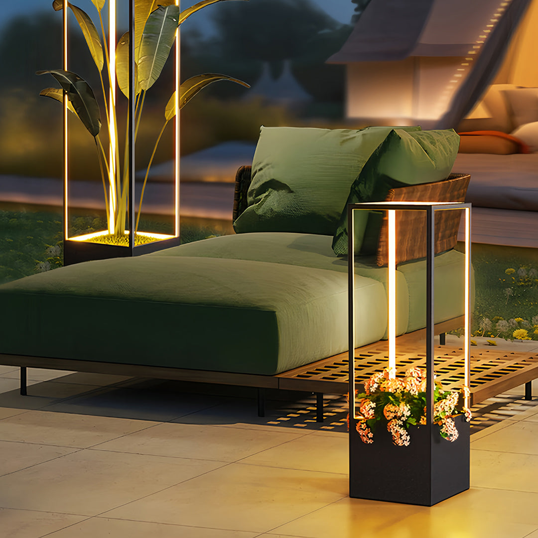 Tall minimalist square floor lamps with an integrated planter, providing warm ambient light next to a chaise lounge on a modern patio.