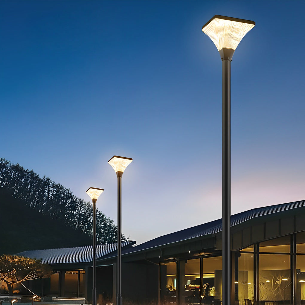 Tall outdoor street lights illuminating a public area near a modern building at night.