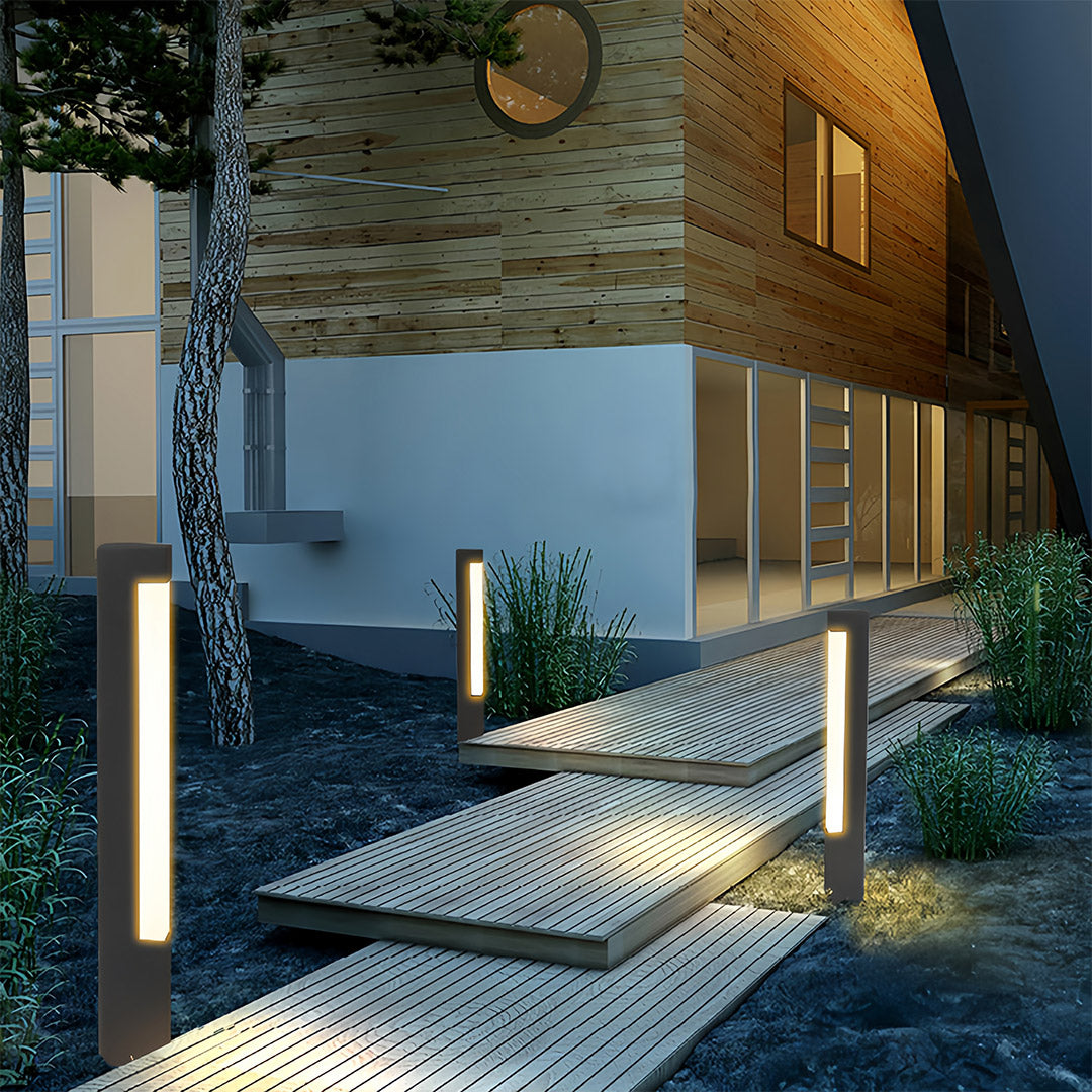 Tall square bollard lights illuminating tiered, anti-slip metal steps and dark landscaping near a house entrance.