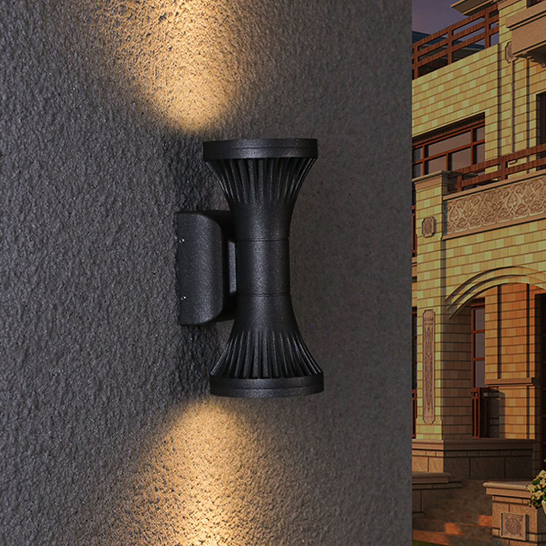 Detailed close-up of the robust textured black finish of the unique hourglass Outdoor Wall Lighting Fixture on a dark stucco wall.