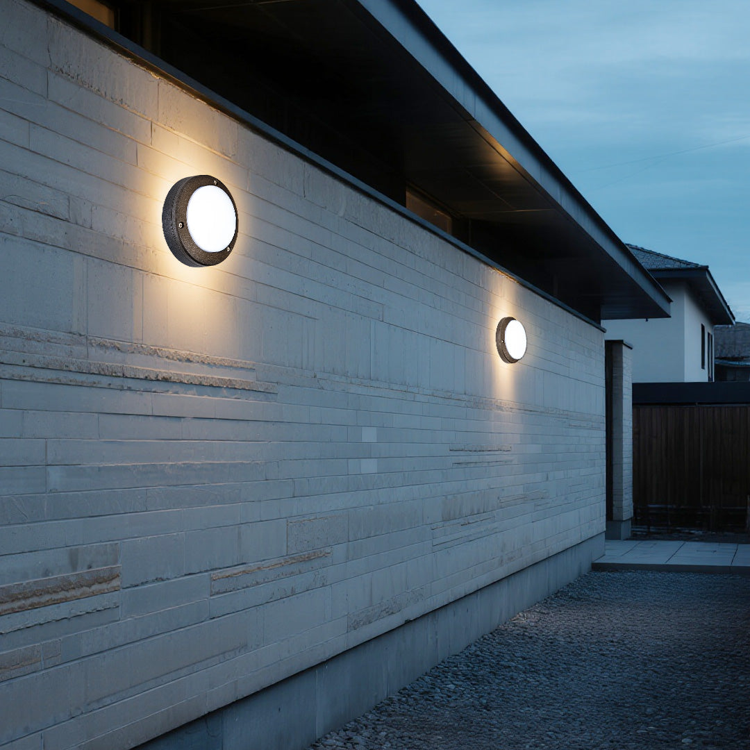 Textured exterior wall featuring two evenly spaced round outdoor wall lights providing ambient illumination along a pathway.