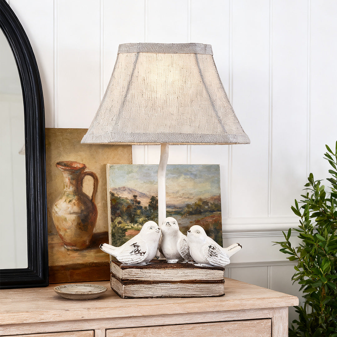 Small bird table lamp featuring a textured shade and whitewashed base, styled next to a tall mirror and oil painting on a dresser.