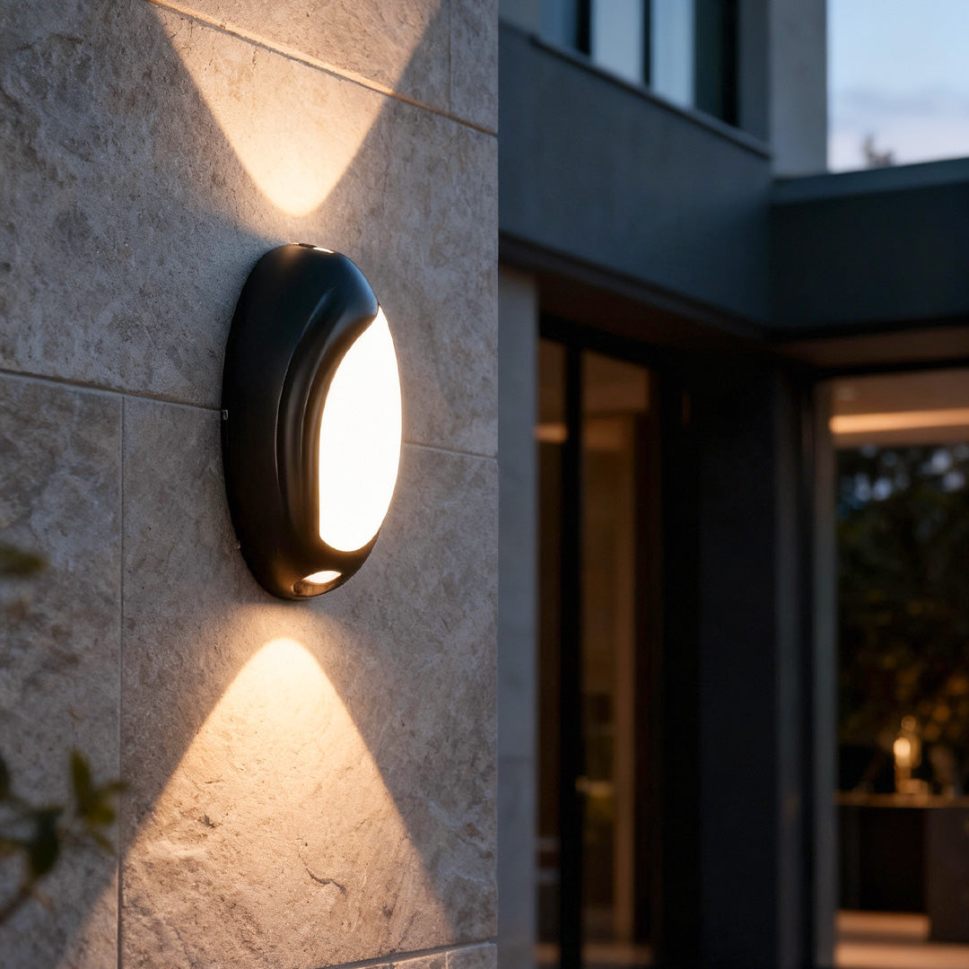 Black modern up down outdoor wall lights illuminating a textured wall at dusk with strong symmetrical light beams.