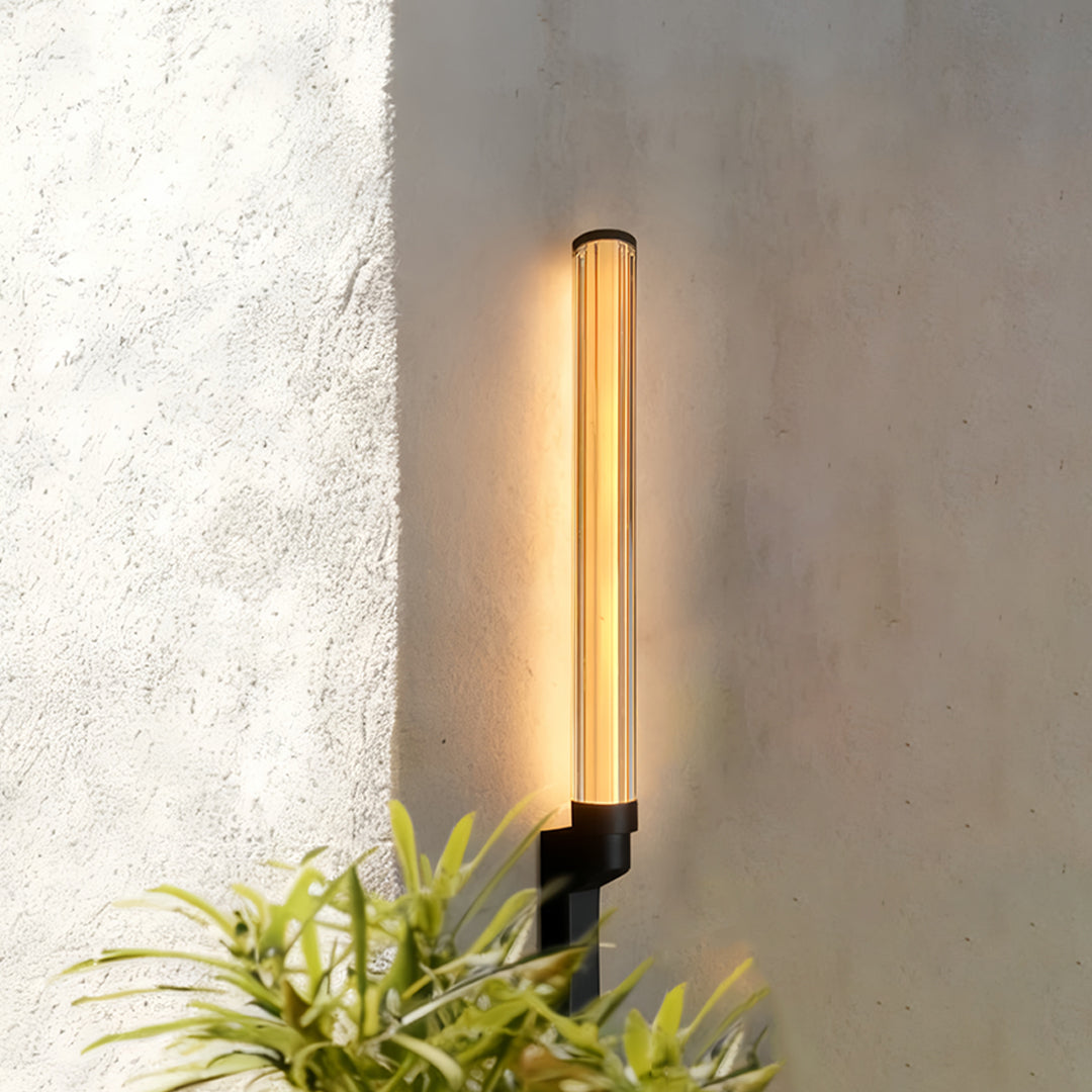 Vertical warm outdoor sconces modern mounted on a textured exterior wall near lush greenery.