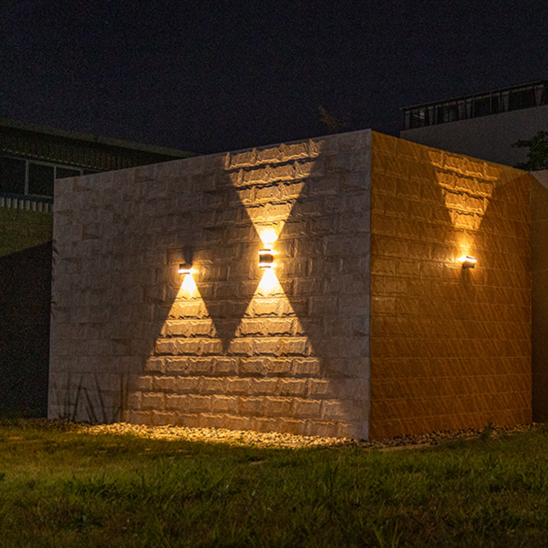 Three black garden wall lights illuminating brick facade at night with warm golden light