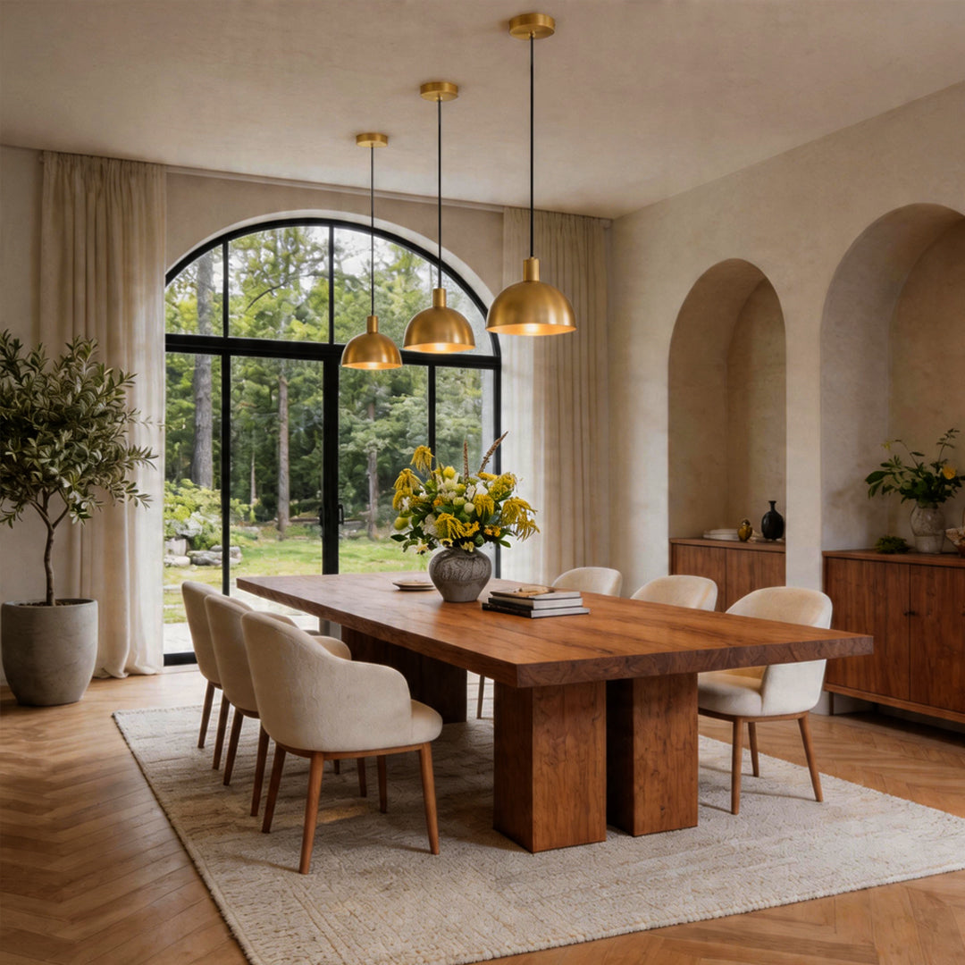 Three brass pendant lighting fixtures glowing over a large rustic wood table in a luxury dining.