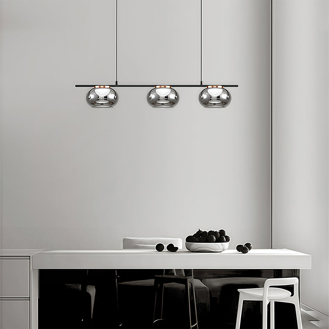 Three gray glass pendant lights arranged in row above modern white kitchen with black bar stools.