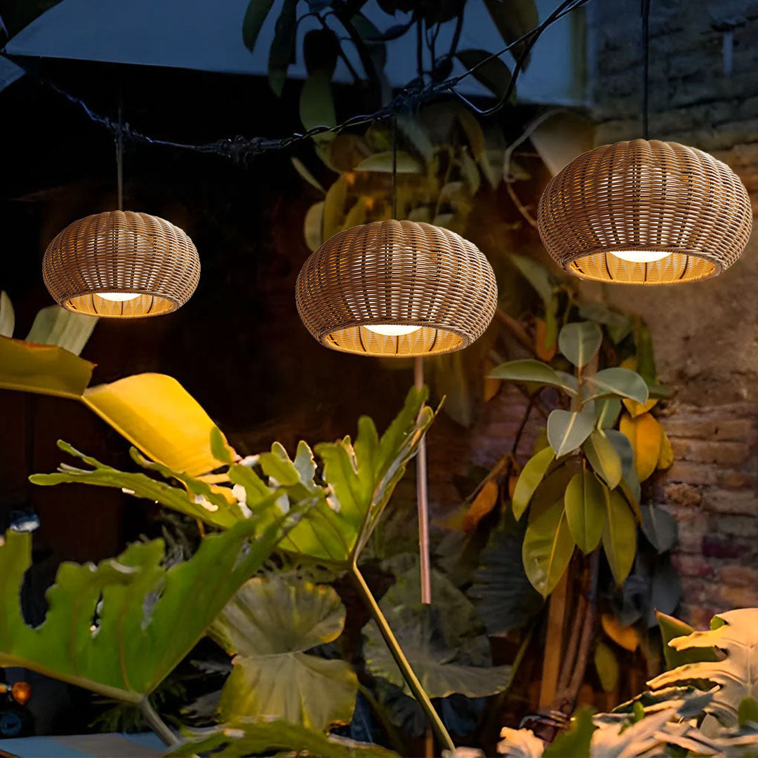 Three rattan outdoor pendant lights hanging among lush green tropical plants during the night.