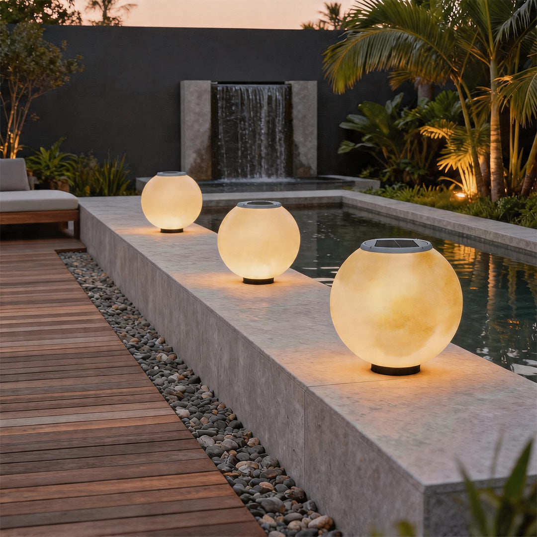 Three solar moon pillar lights illuminating a stone pool edge next to a tropical garden pond.