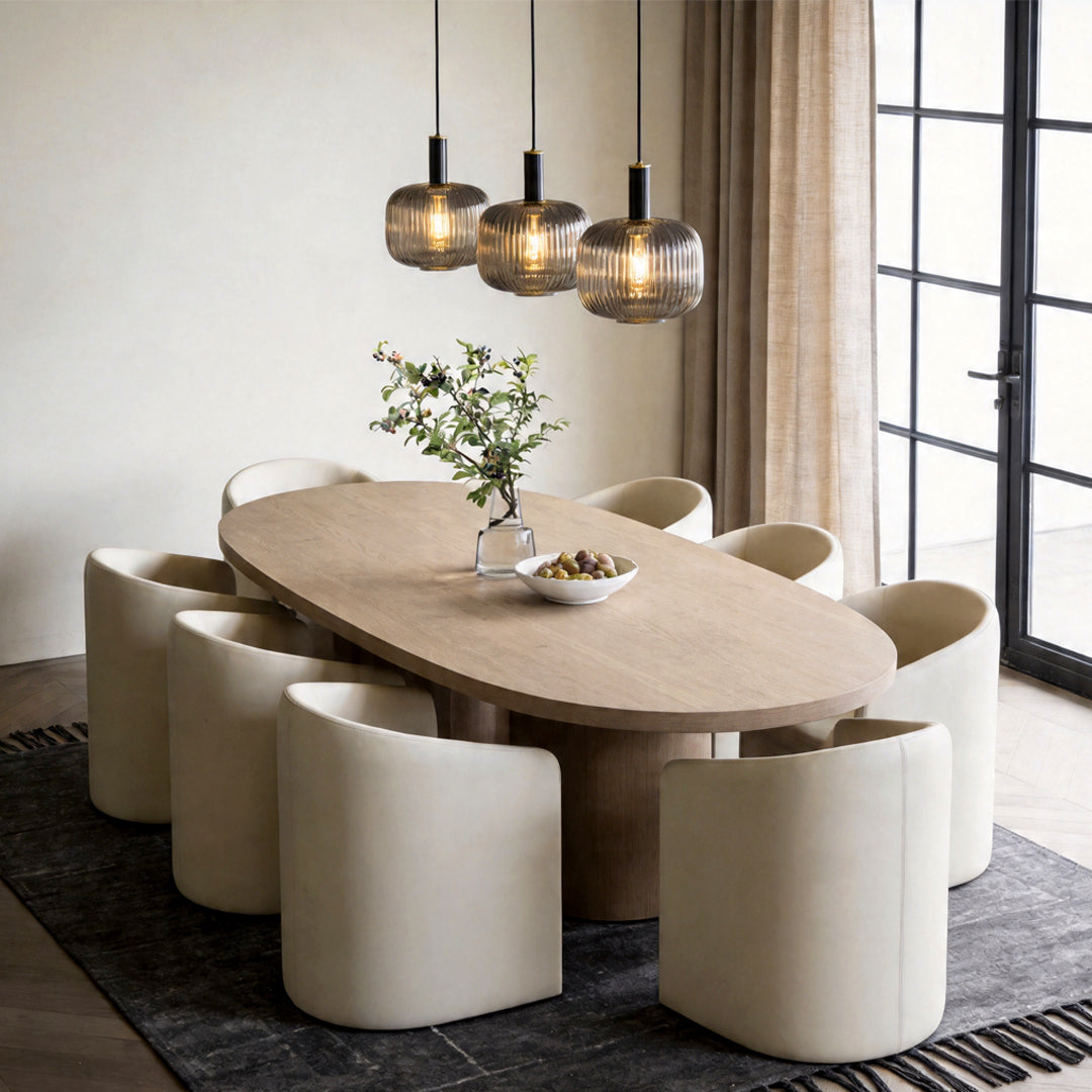 Three vintage glass pendant light fixtures hanging above a luxury oval dining table and chairs.