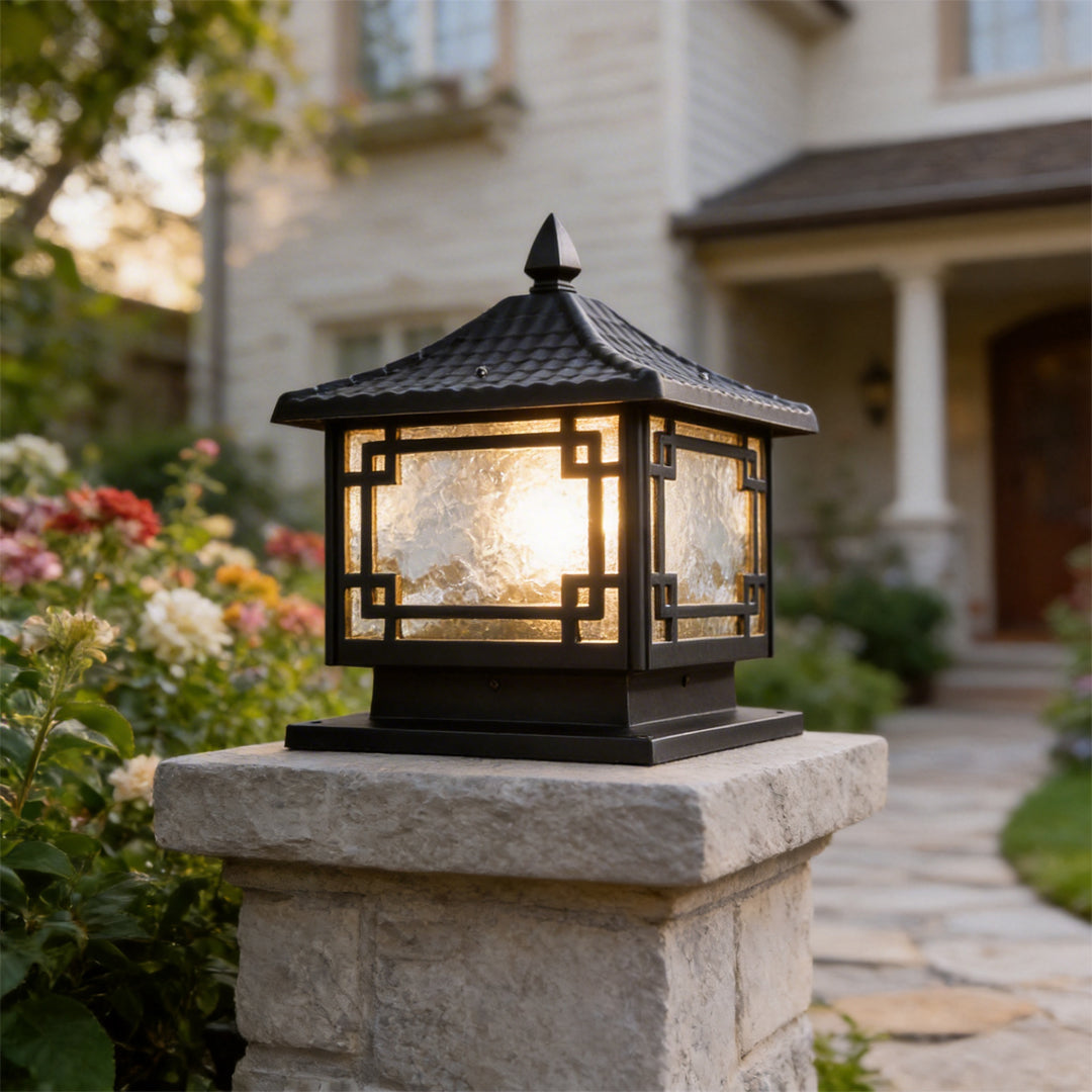 Traditional black outdoor garden pillar lights glowing on a stone post by a house garden path.