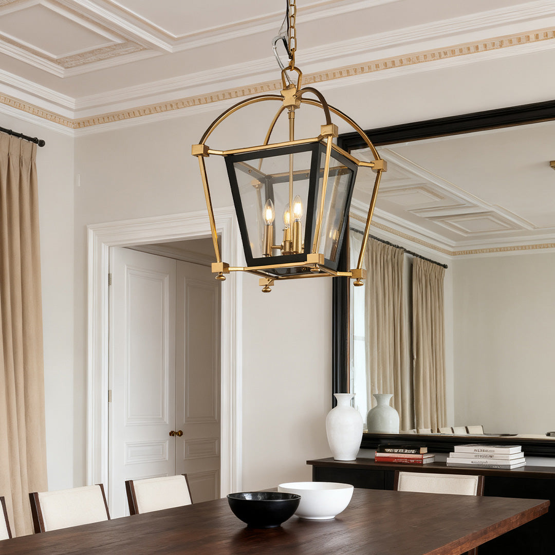 Traditional gold lantern pendant light suspended over a dark wood dining table in a formal room with decorative white molding.