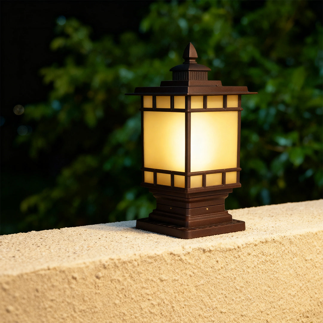 Traditional metal pillar light with frosted panels emitting warm ambient glow on stone surface at dusk