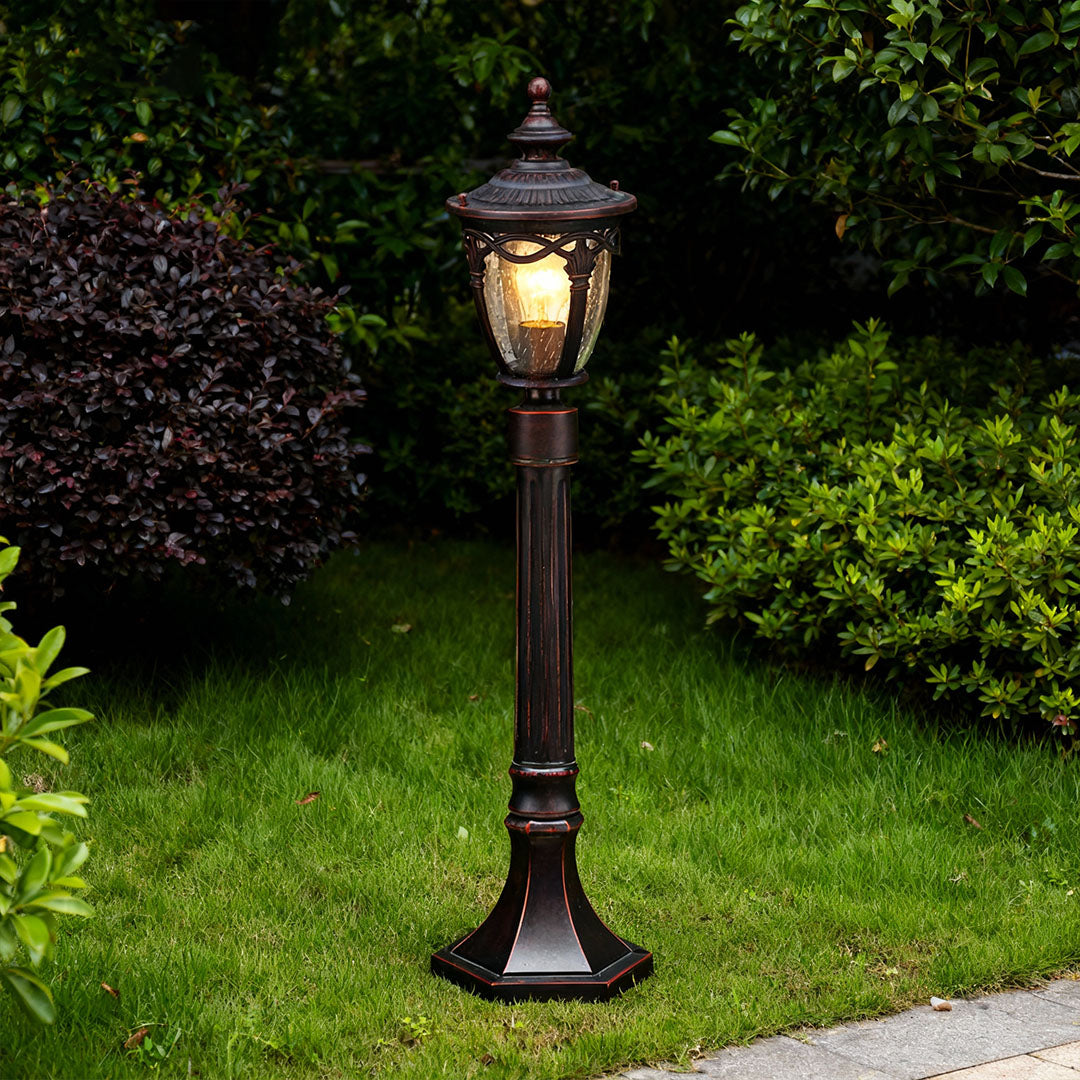 Traditional outdoor light bollard casting glow on grass beside residential curved pathway at evening