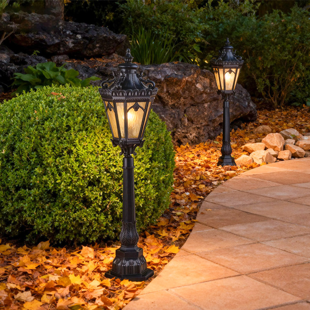 Traditional pathway lighting bollard illuminating curved walkway covered with autumn leaves at dusk