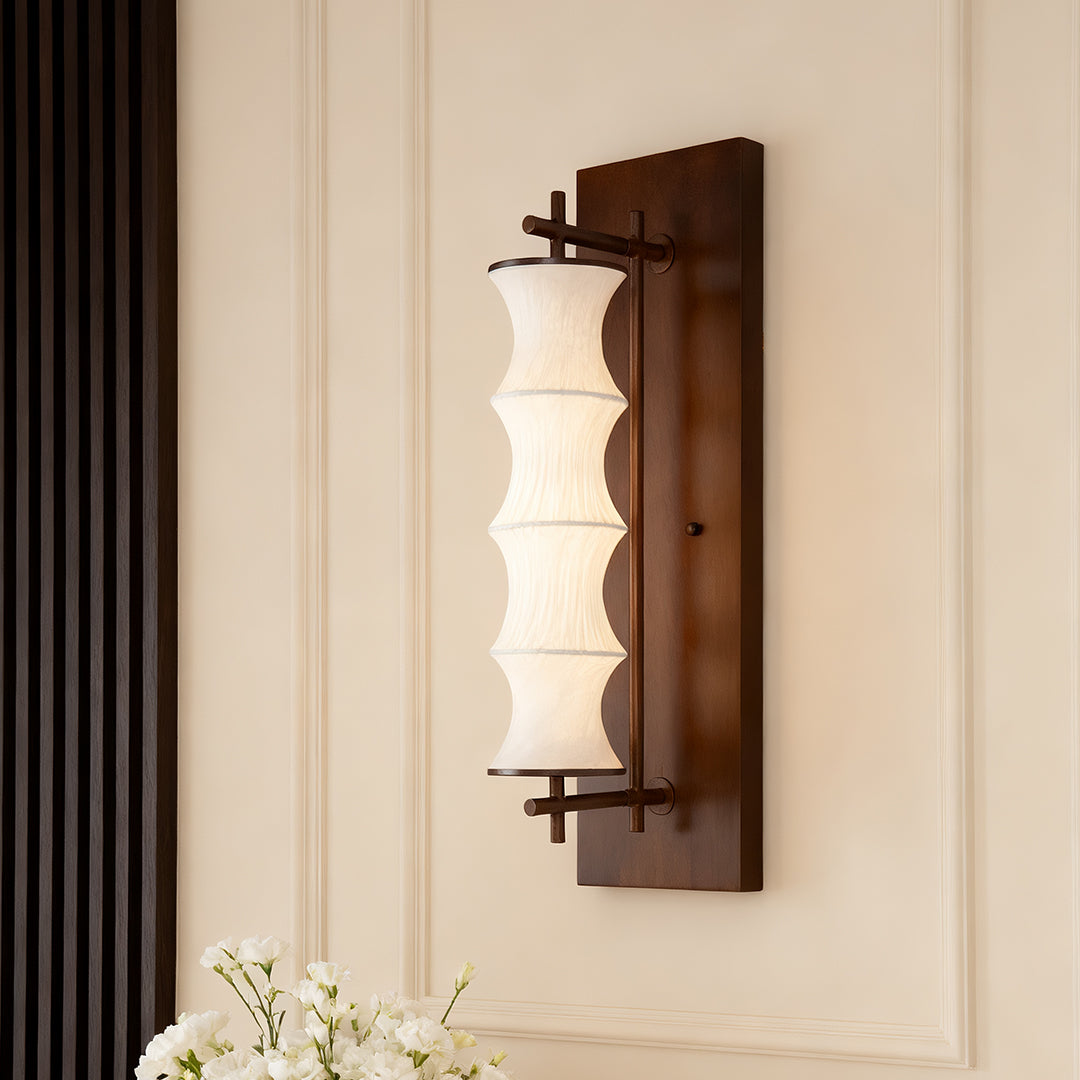 Traditional vintage light wall sconce with a tiered fabric shade and dark wood backplate, providing soft accent lighting in a living space.