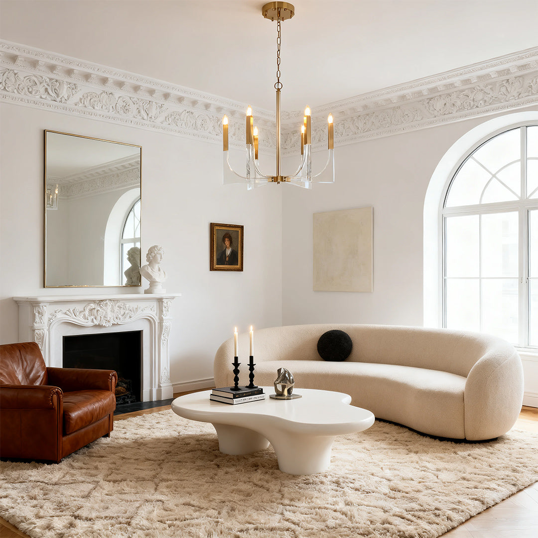 Traditional-style acrylic chandeliers with transparent base elements, complementing a white fireplace and ornate molding in a formal sitting room.